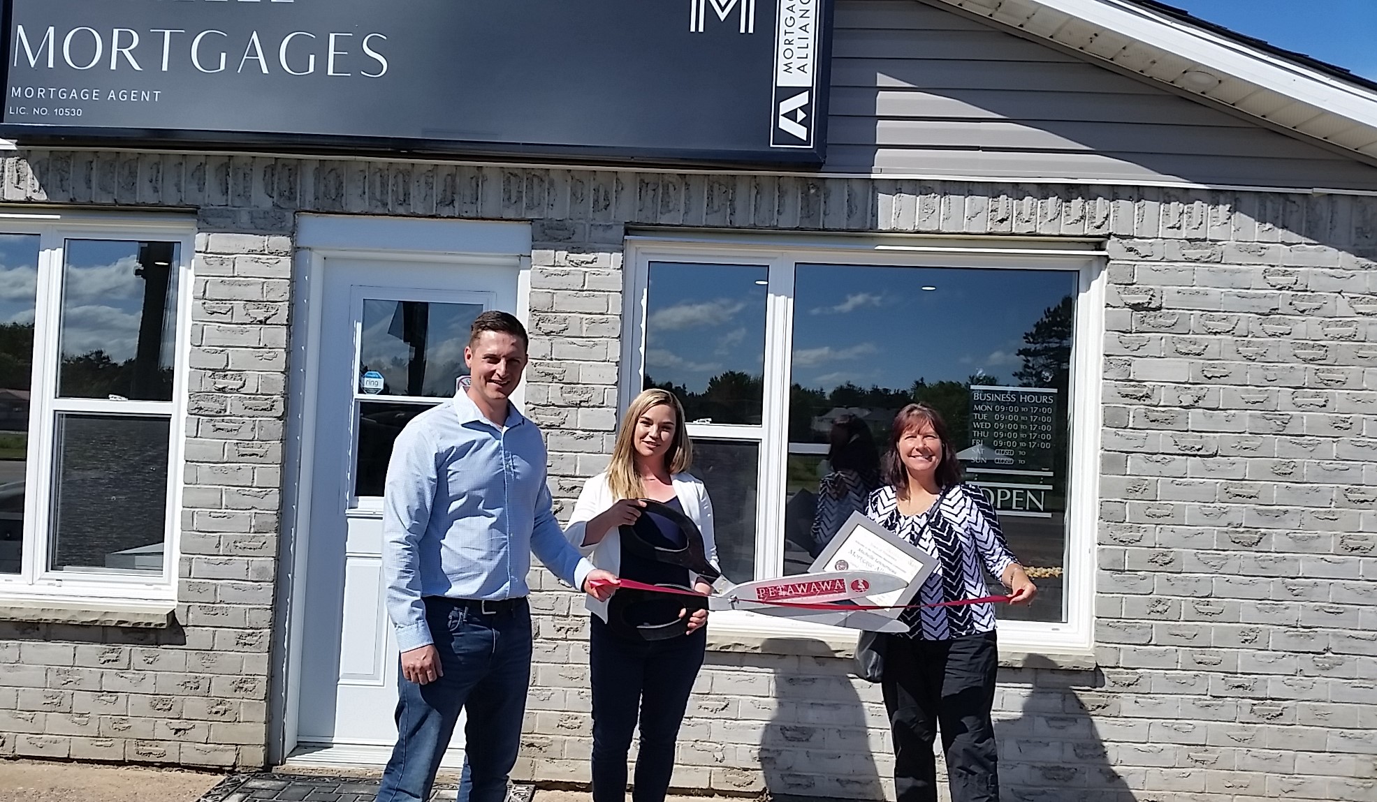 man and two women in front of building with giant scissors