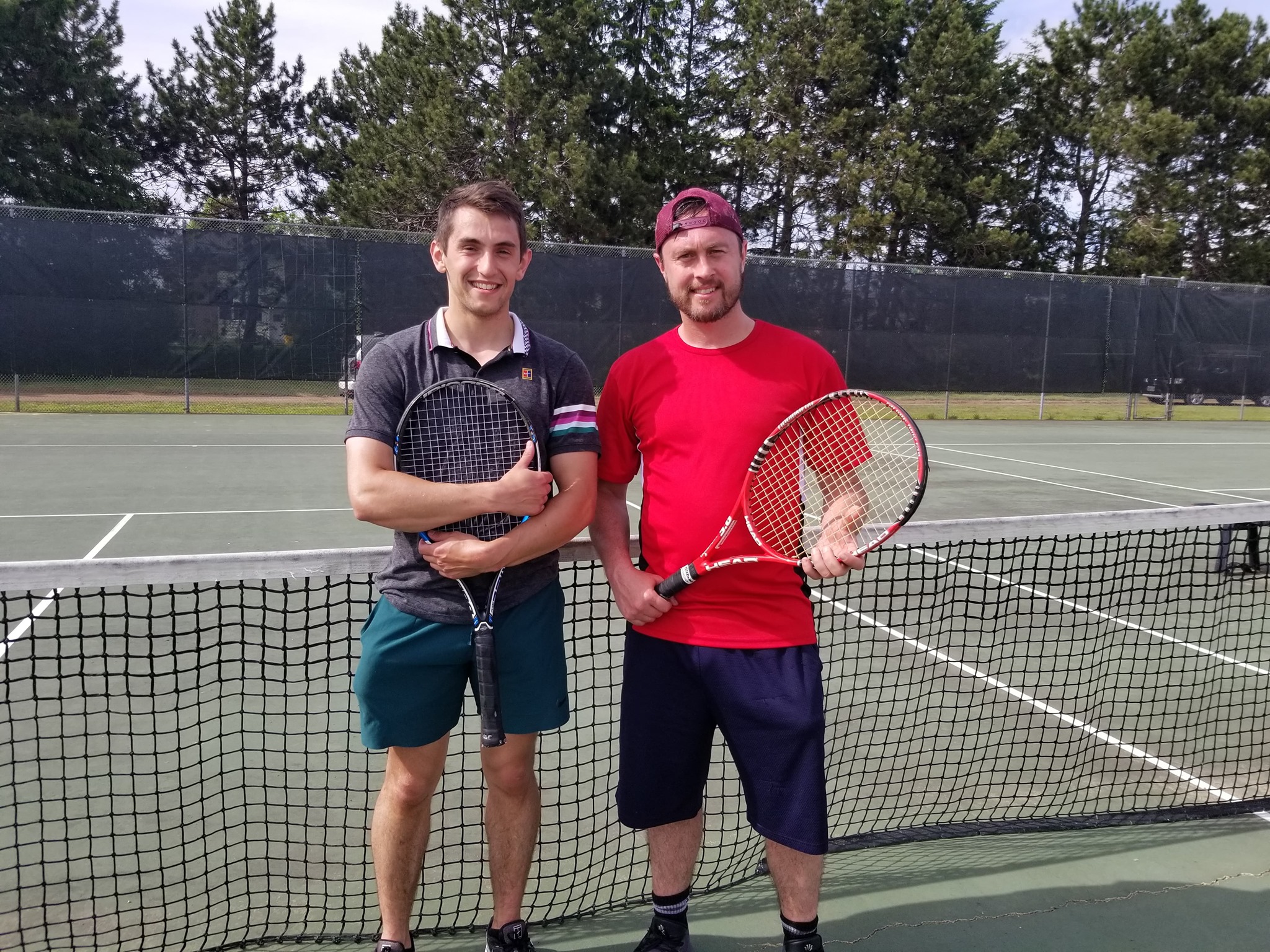 Photo of 2 men holding tennis requests with tennis court in background