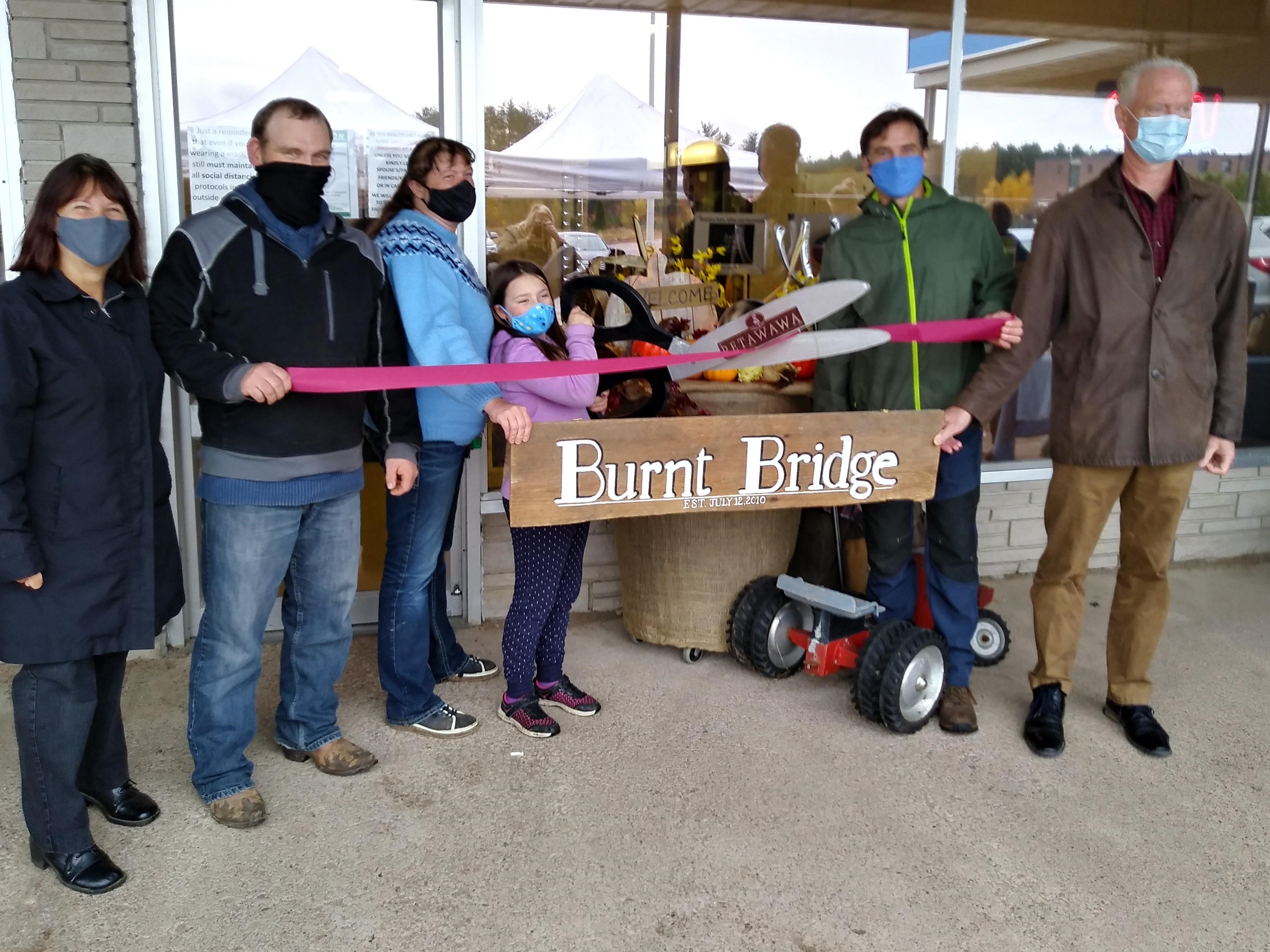 A group of people with giant scissors cutting a burgundy ribbon