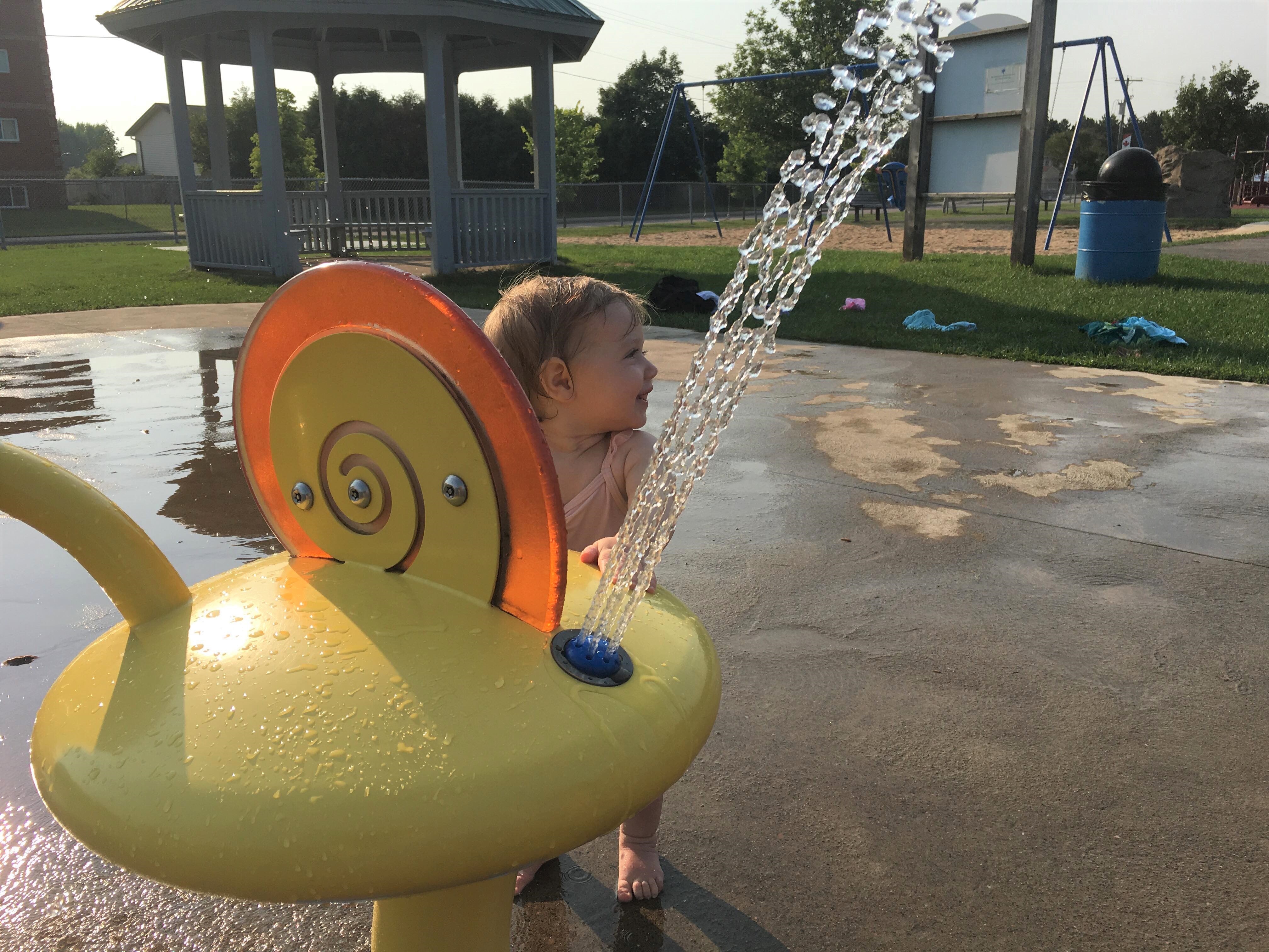 photo of a small child playing under the water sprays at the splash pad
