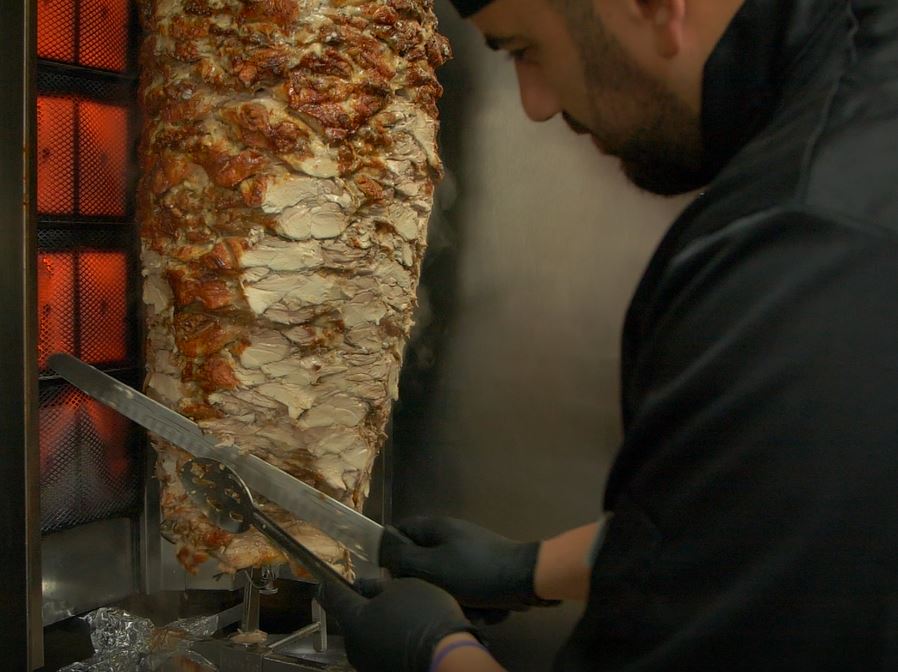 a shawarma in circulation being cut by a chef 